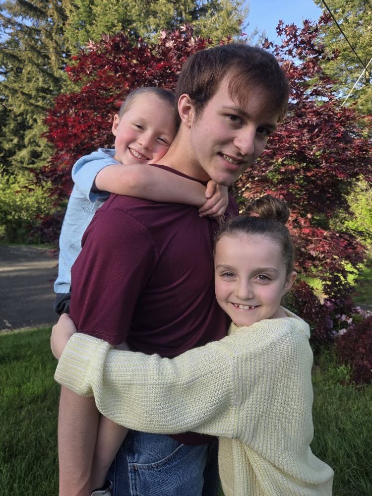 Ayden giving a piggyback ride to a little boy while a little girl hugs him