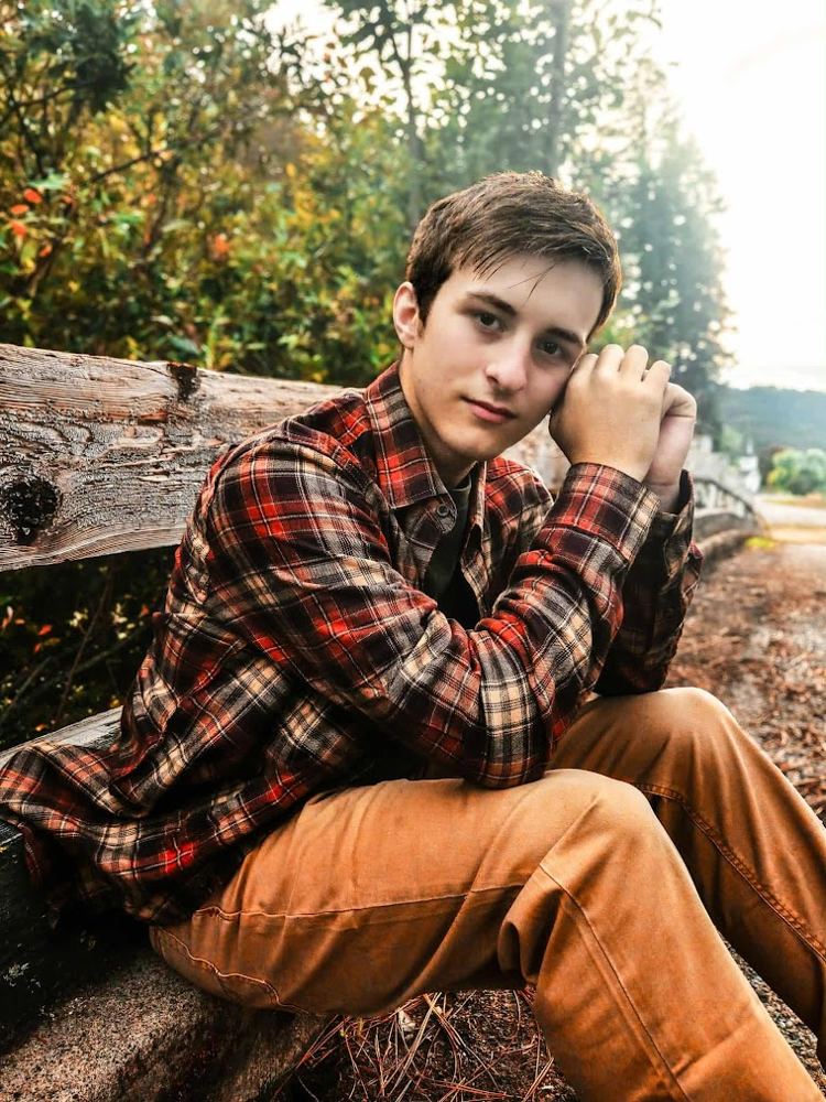Ayden sitting on a wooden fence in a plaid shirt for his senior photo