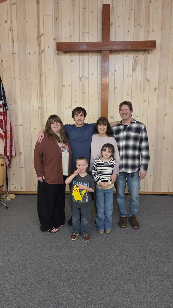 Family photo of six people standing in front of a wooden cross