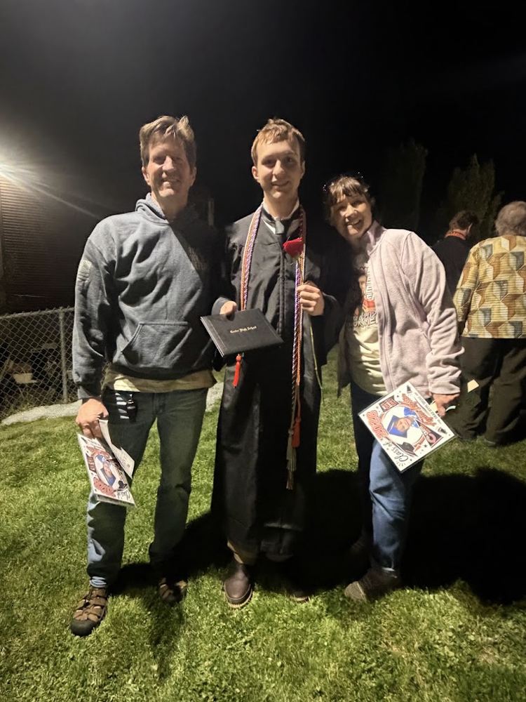 Ayden in his graduation gown holding his diploma, with two family members
