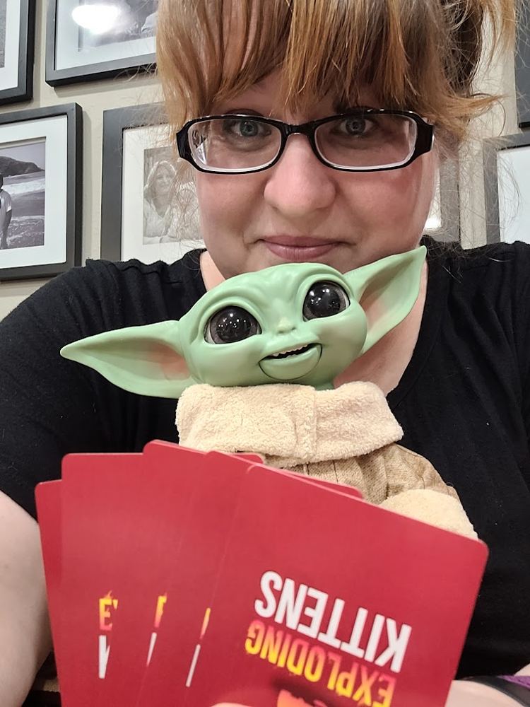 Logston holding a baby alien toy and Exploding Kittens cards